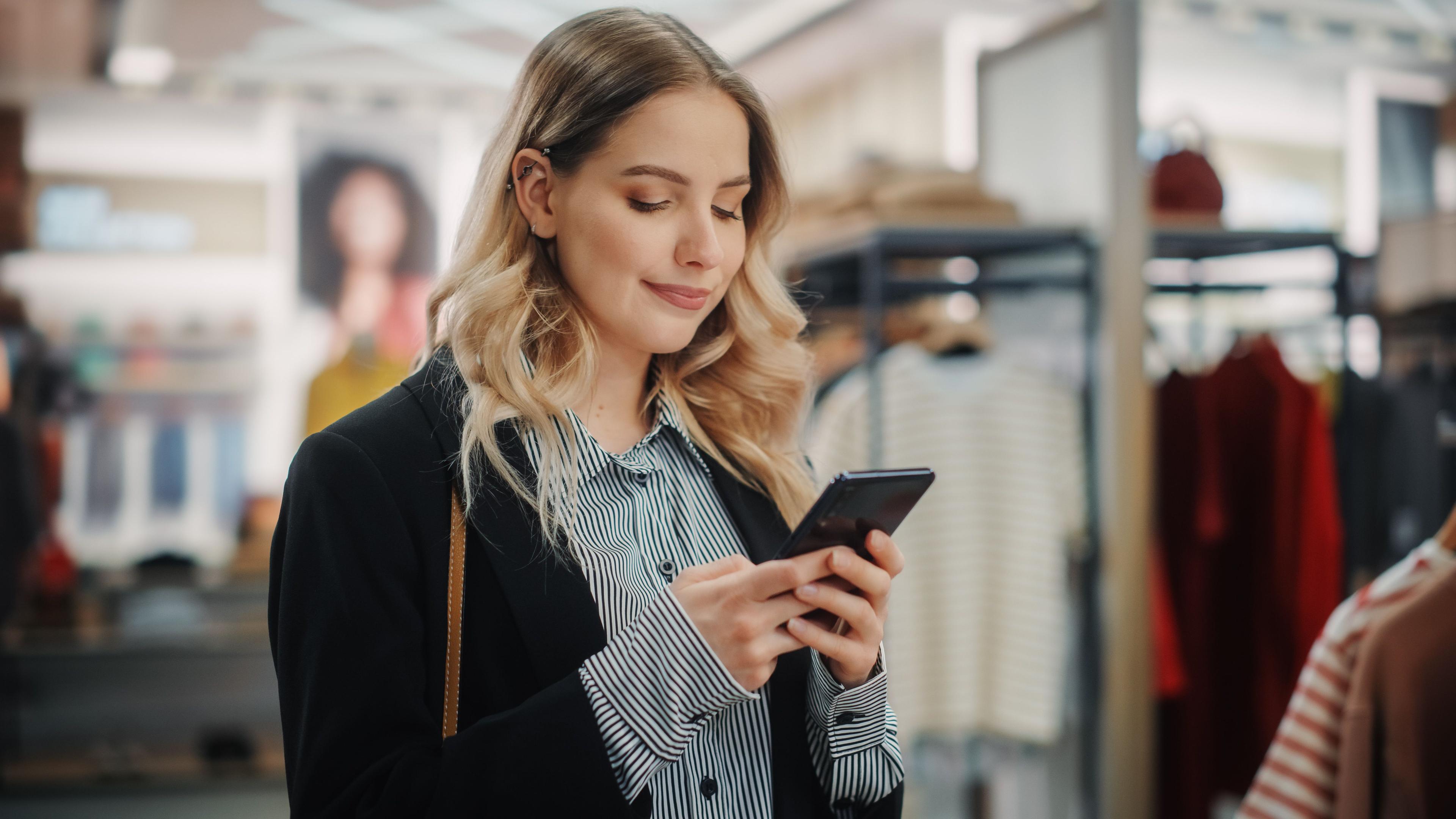 Junge Frau im Modegeschäft blickt auf ihr Smartphone
